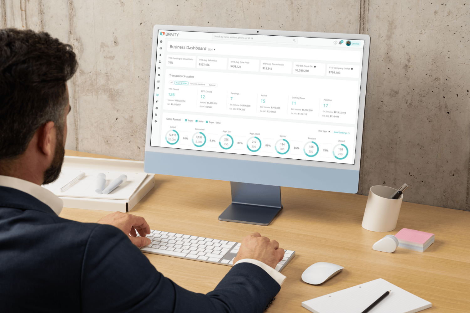 Close-up of a computer screen showing a real estate CRM dashboard with charts, lead tracking, and team accountability metrics, with an agent analyzing the data.